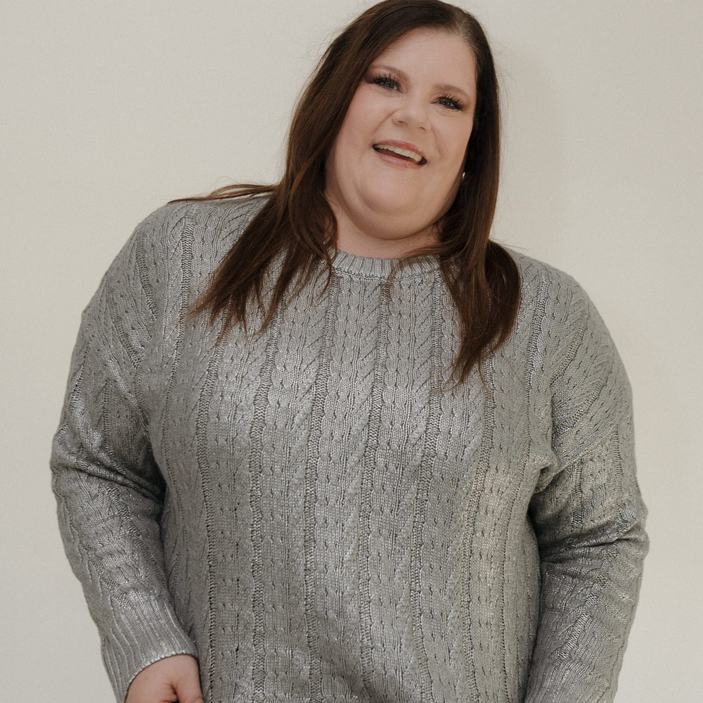 Person wearing a gray cable knit sweater against a plain background