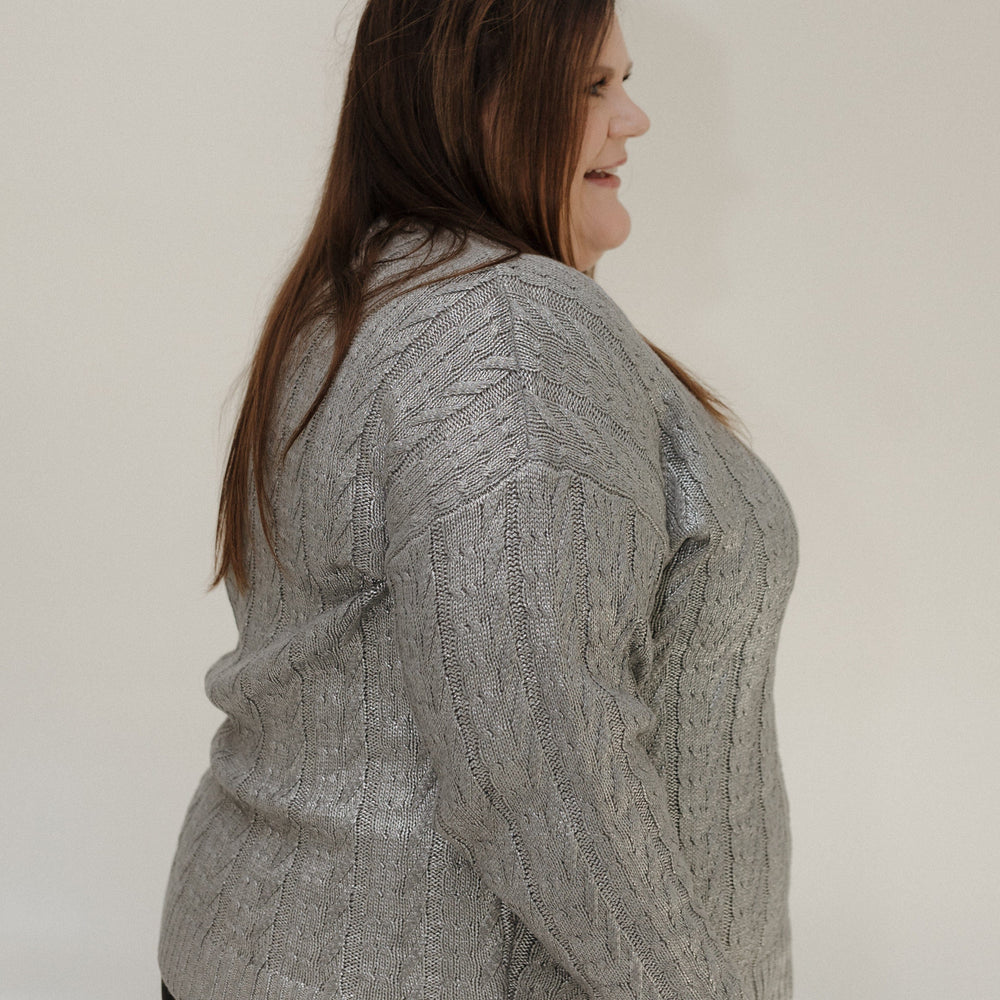 Woman wearing a gray cable knit sweater against a plain background