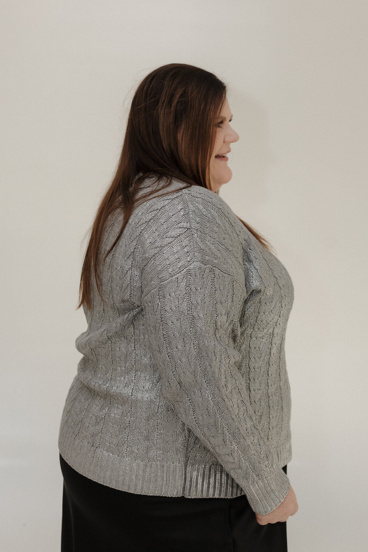 Woman wearing a gray cable knit sweater against a plain background