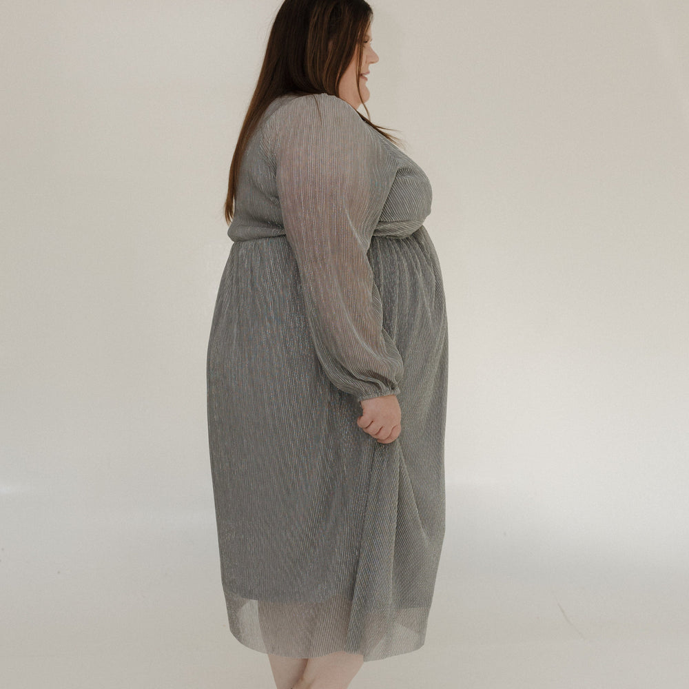 Woman wearing a gray dress standing against a white wall