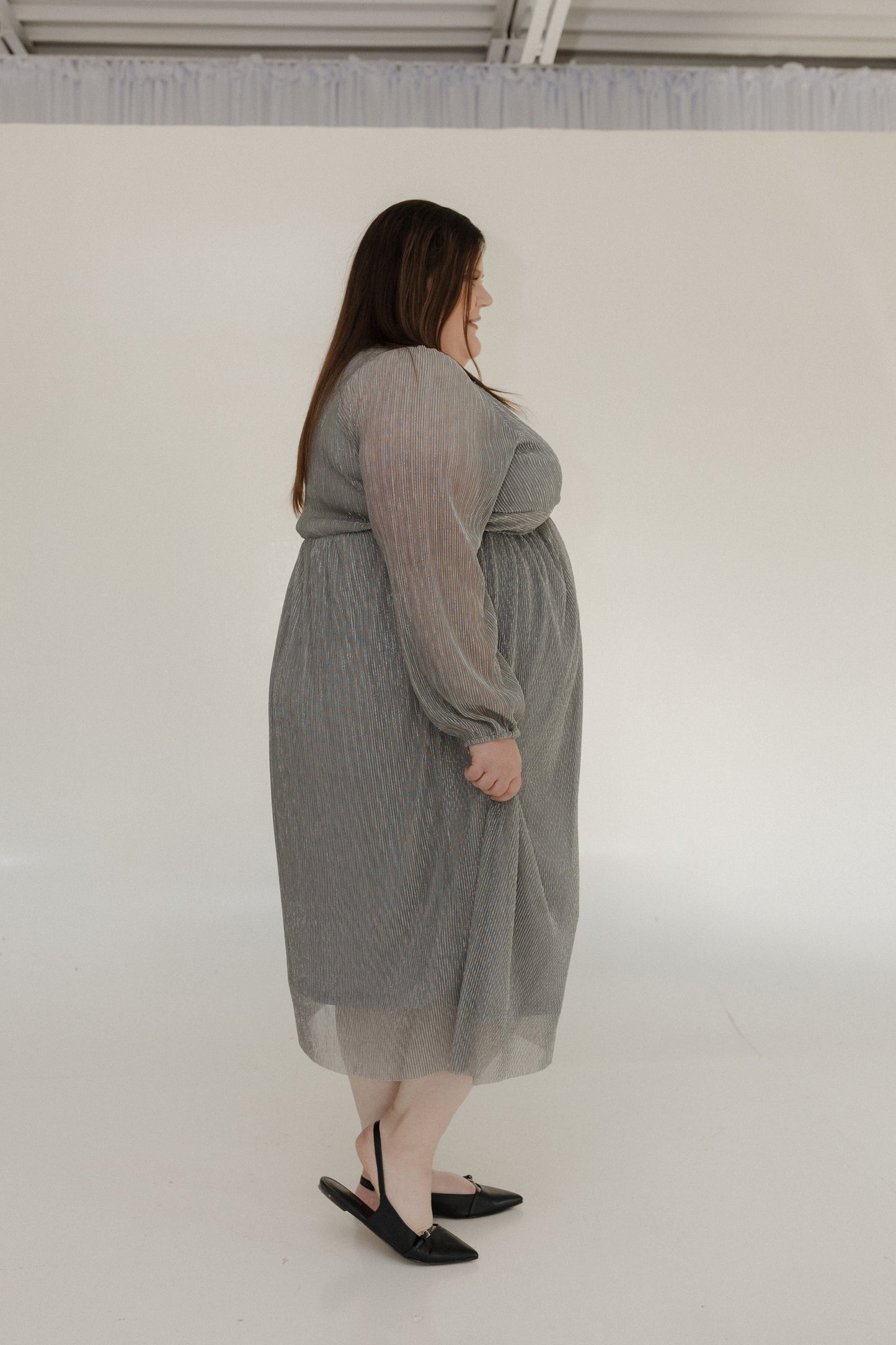 Woman wearing a gray dress standing against a white wall
