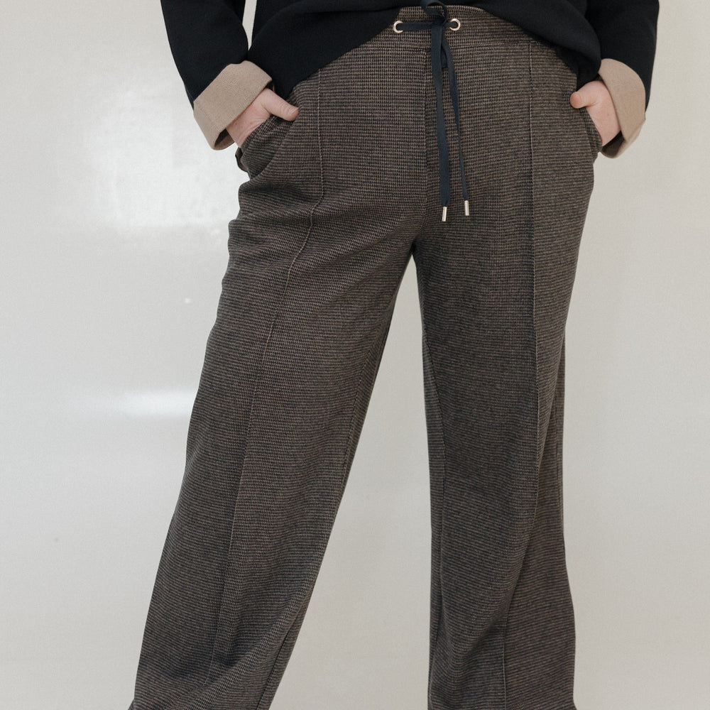 Person wearing brown checkered pants with a black top on a white background