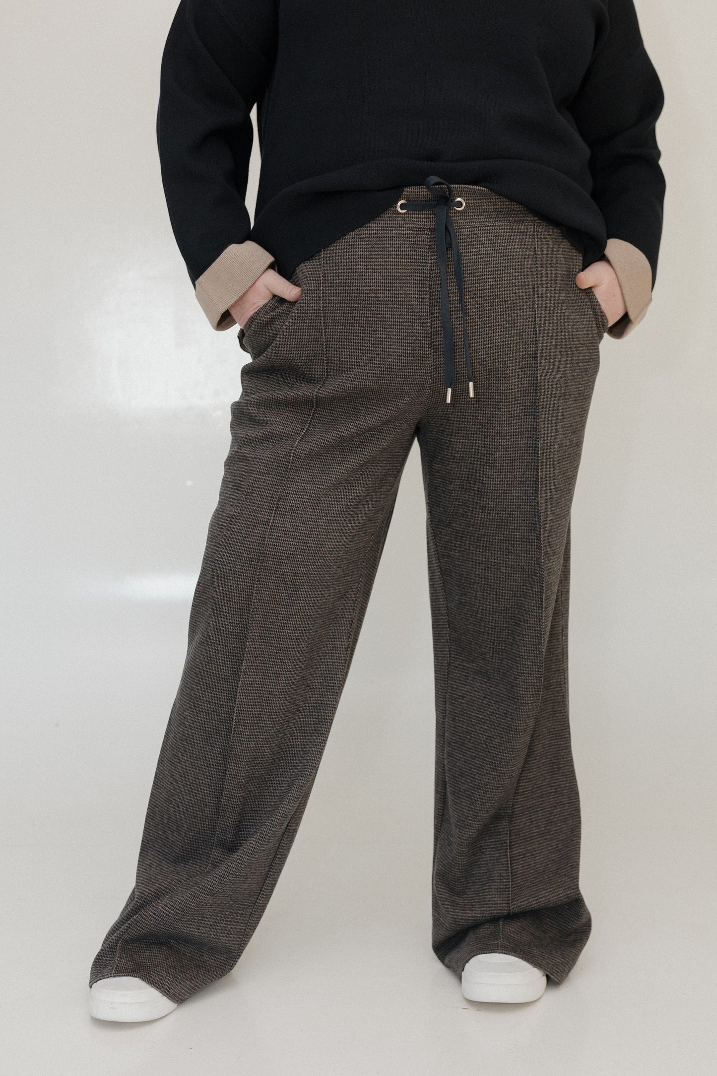 Person wearing brown checkered pants with a black top on a white background