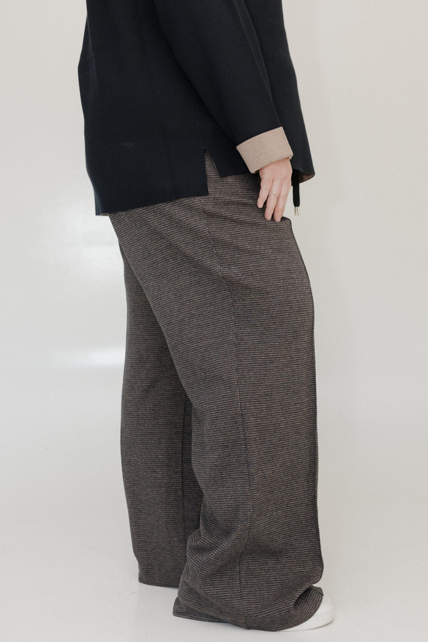 Person wearing a black coat and gray checkered pants on a white background