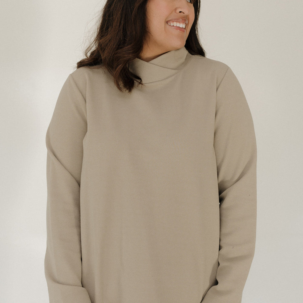 Woman wearing a beige turtleneck sweater against a white background