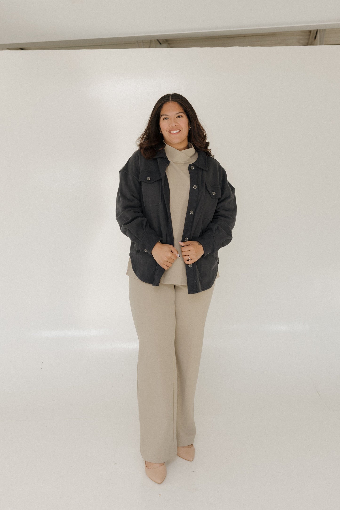 Woman wearing a dark jacket, beige turtleneck, and pants on a white background