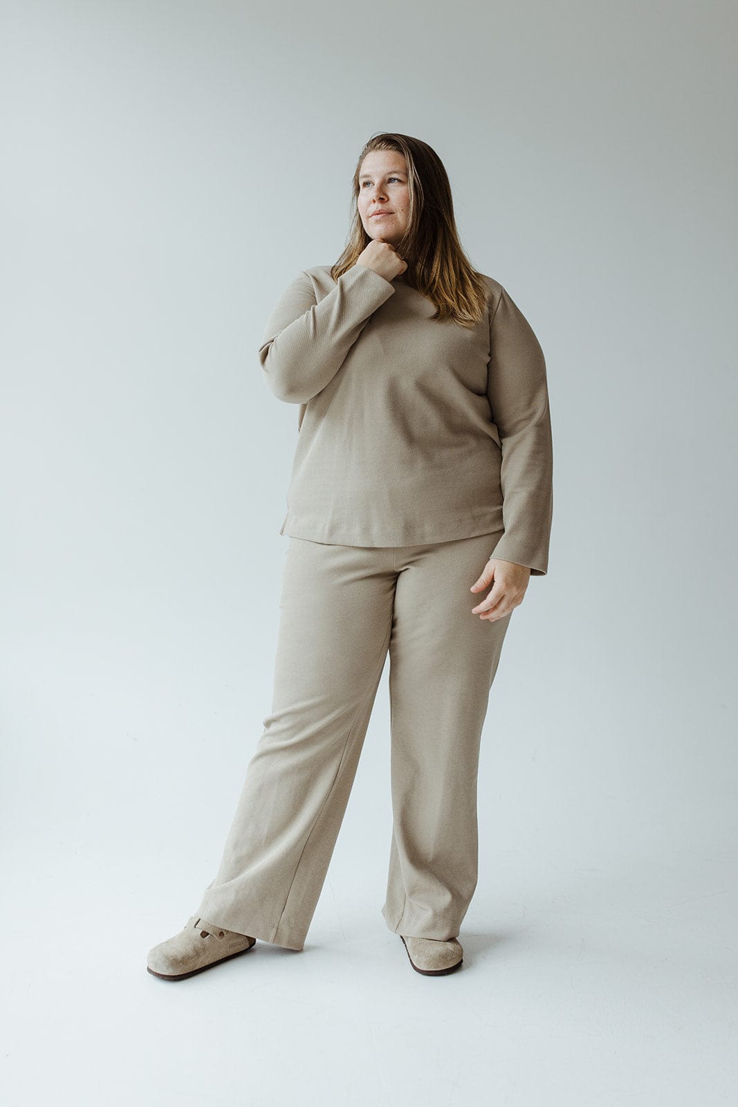 A person stands against a plain background, wearing the LIGHT KHAKI STRAIGHT LEG PULL-ON PANT from Yesta and comfortable slippers, with one hand touching their neck.