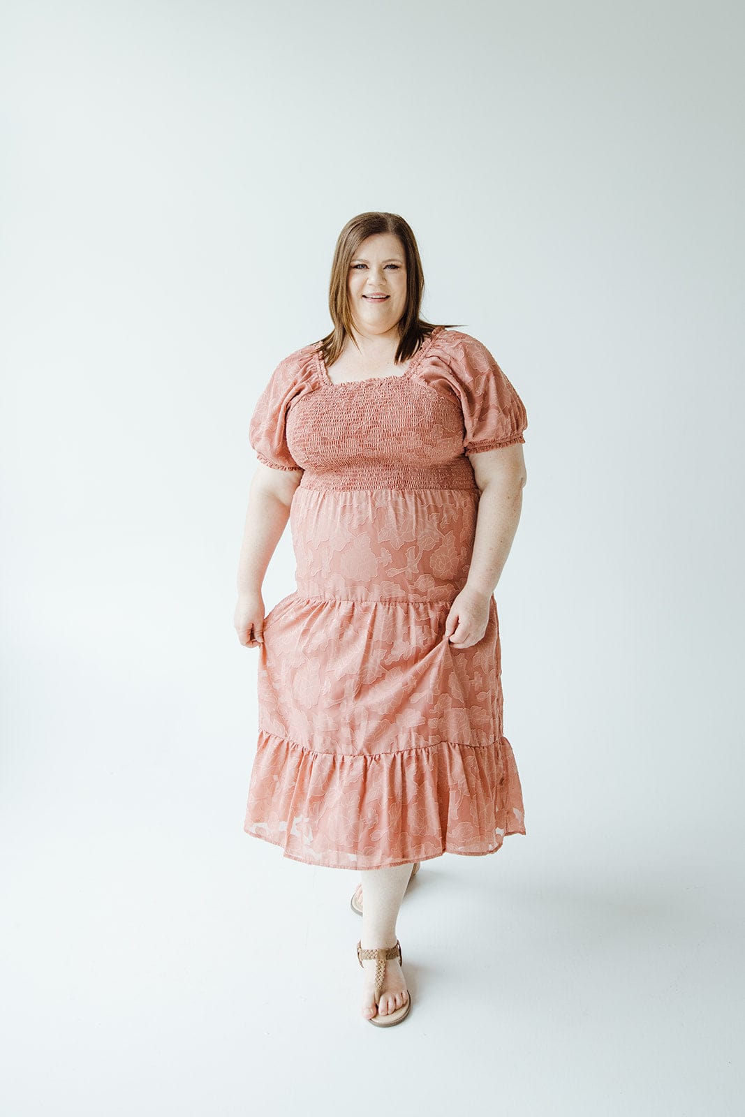 A woman wearing a MIDI-LENGTH LACE APPLIQUES IN PRESSED FLOWER dress by Mikarose stands against a plain white background.