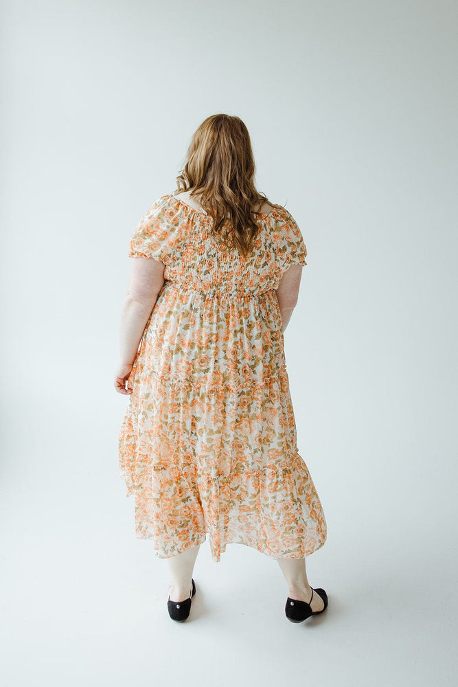 A person with long hair in a Mikarose MIDI-LENGTH FLORAL DRESS WITH BUBBLE SLEEVE stands facing away from the camera against a plain, light-colored background.