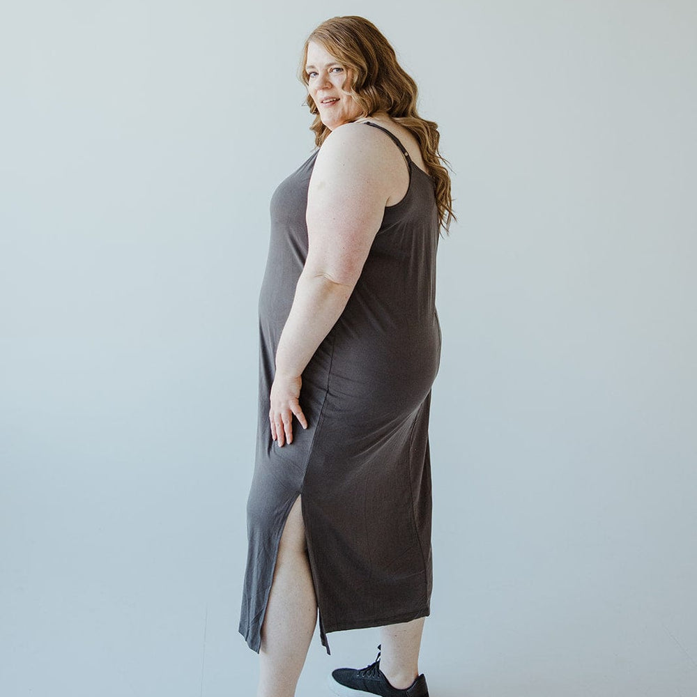 A woman in a dark modal fabric midi dress with adjustable cami straps and black sneakers poses sideways against a light background.