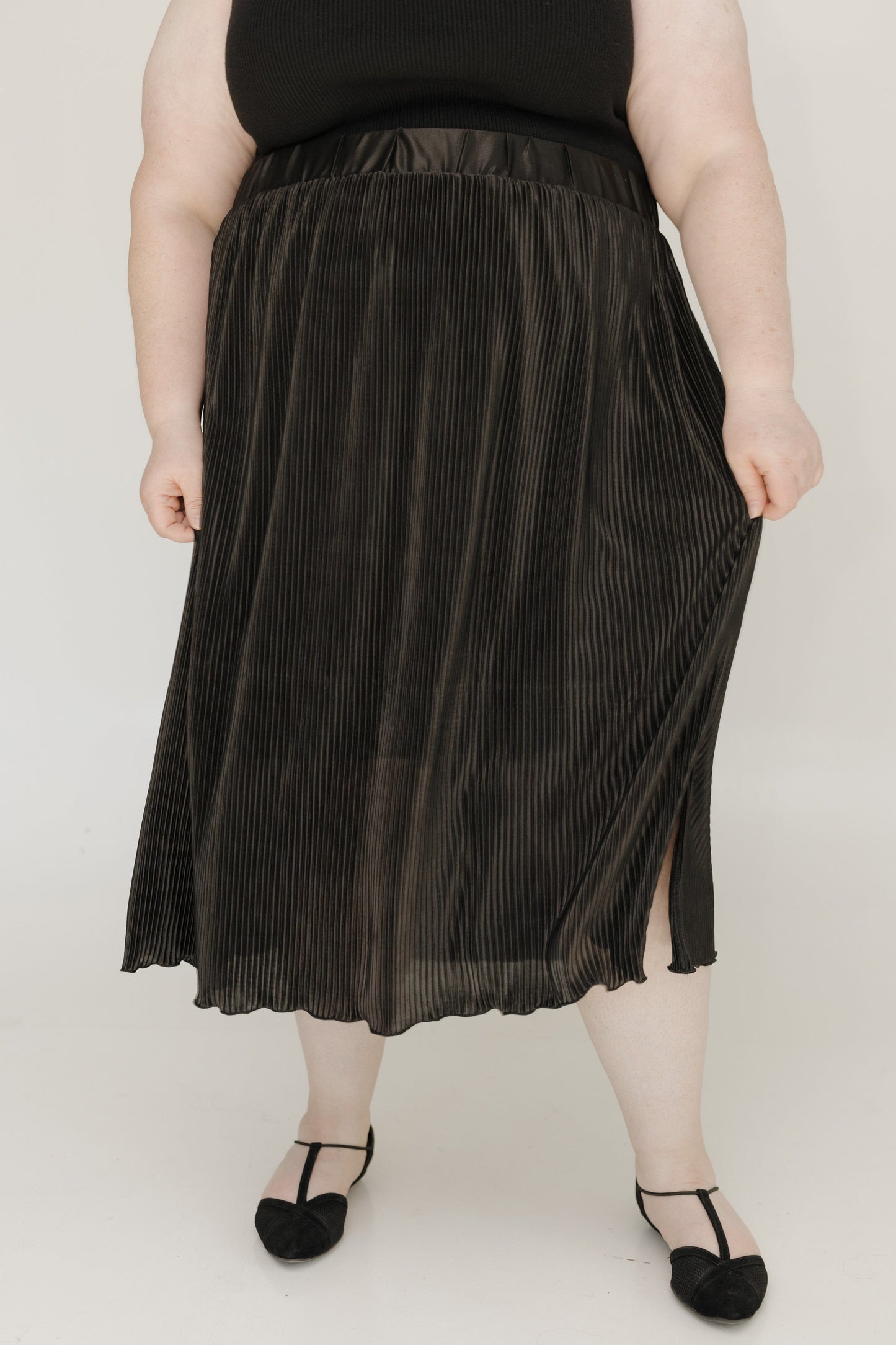 Person wearing a black pleated skirt on a plain background