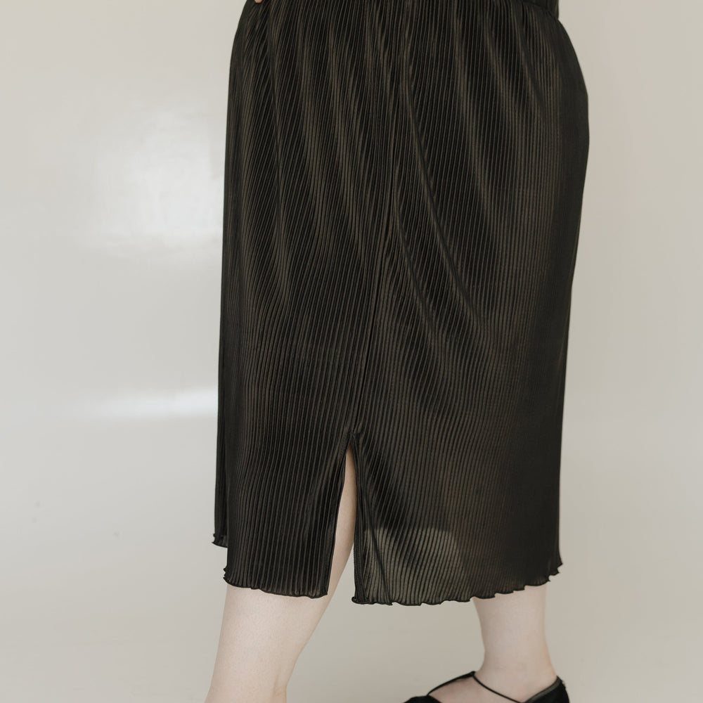 Person wearing black pleated pants and black shoes on a plain background