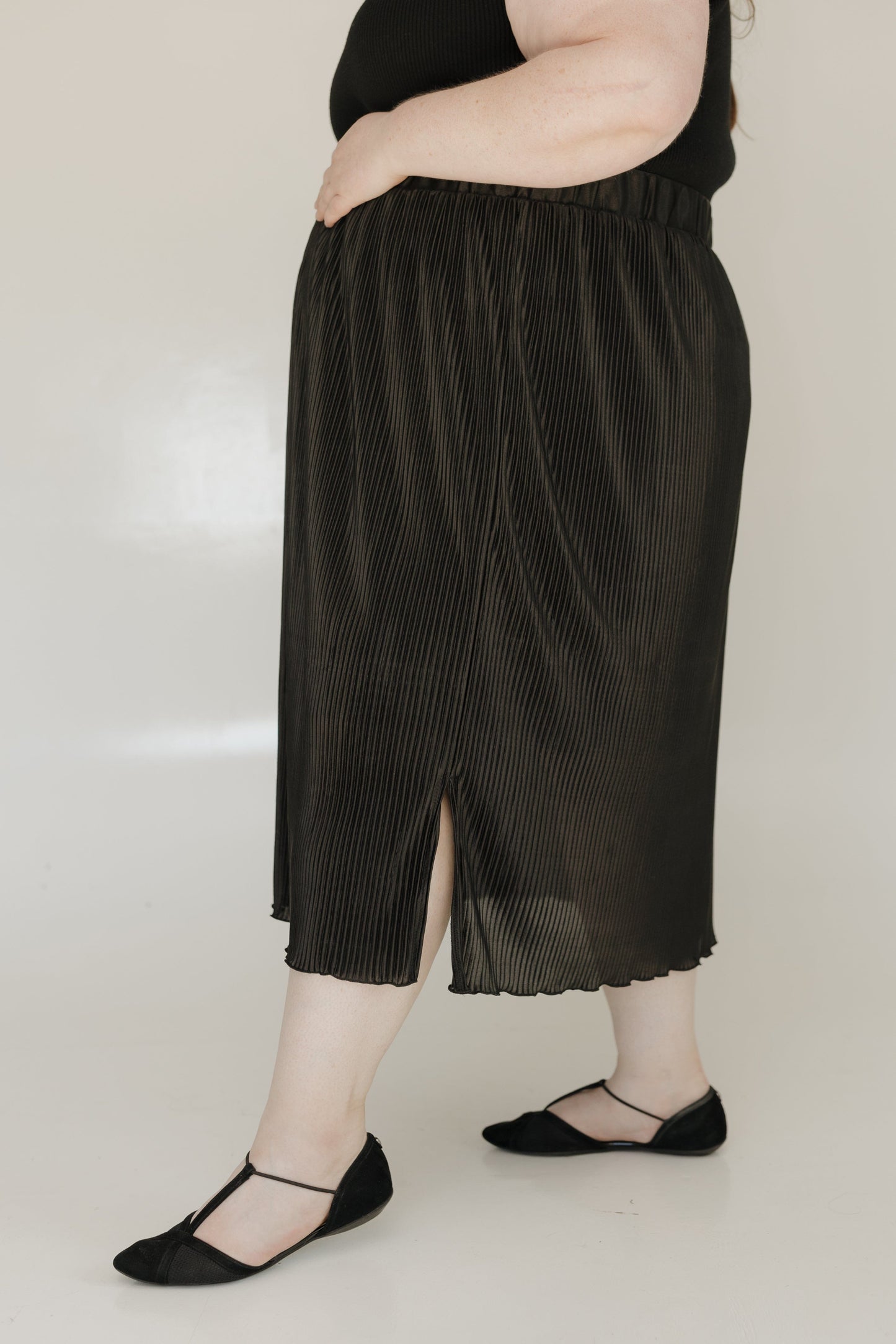 Person wearing black pleated pants and black shoes on a plain background