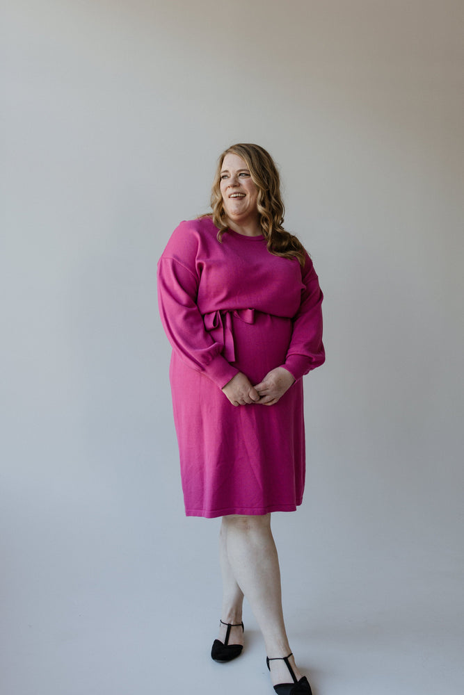 A person in a fuchsia rose MIDI LENGTH SWEATER DRESS by Yesta, featuring bubble sleeves, stands with hands clasped and smiling against a plain background.