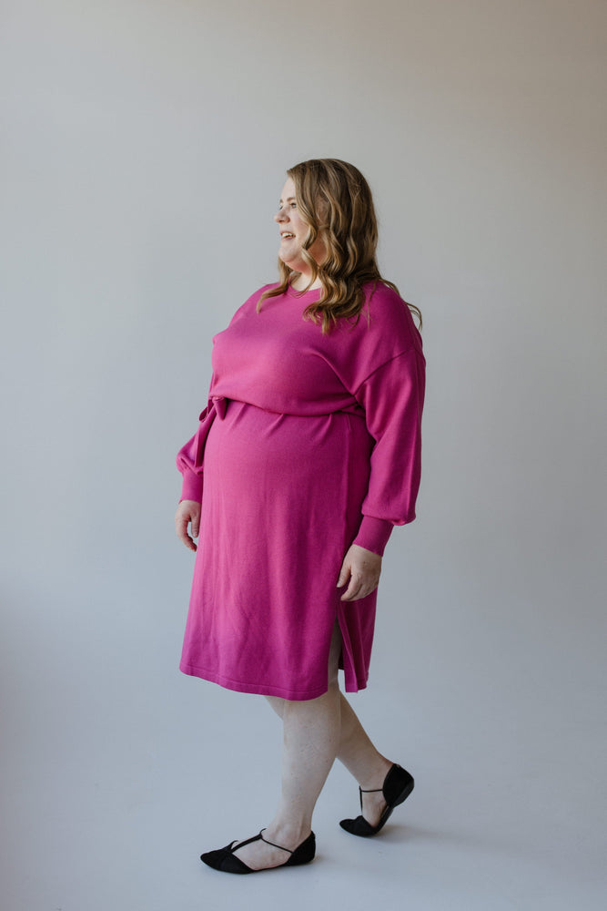 A person in a fuchsia rose MIDI LENGTH SWEATER DRESS, designed by Yesta, featuring long bubble sleeves and a ribbon tie detail.