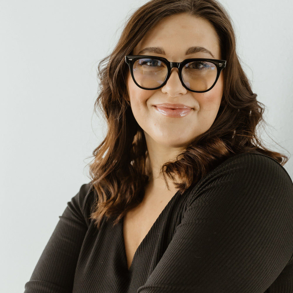 Woman wearing glasses and a dark top against a light background