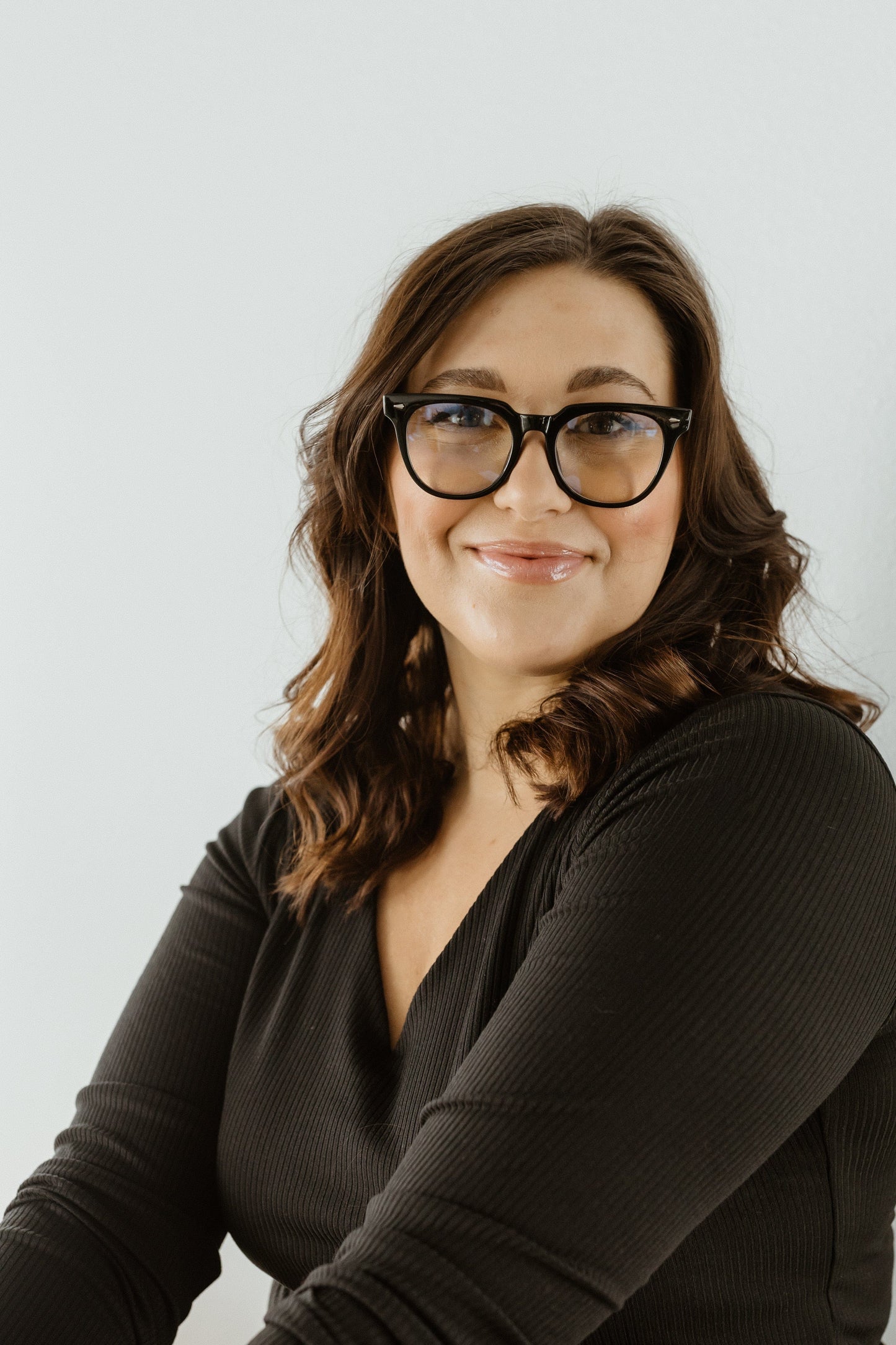 Woman wearing glasses and a dark top against a light background