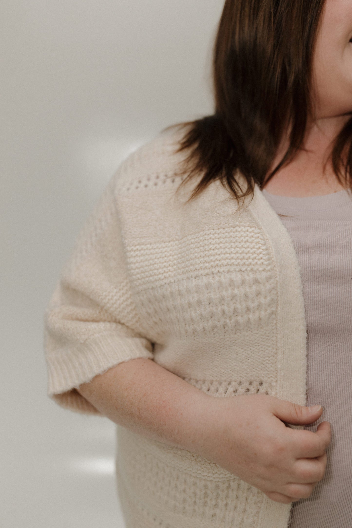 Person wearing a beige knitted cardigan against a plain background