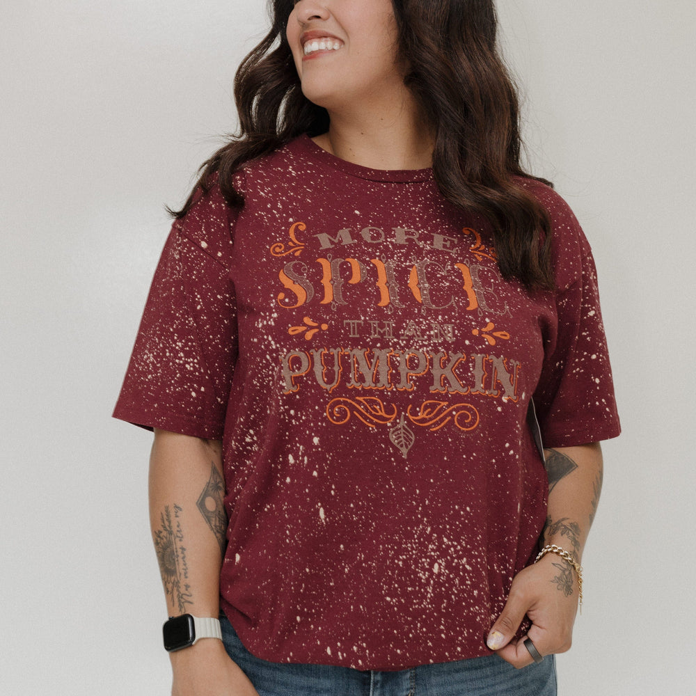 "MORE SPICE THAN PUMPKIN" GRAPHIC TEE Woman wearing a maroon shirt with 'More Spice Than Pumpkin' text on a plain background at Love Marlow