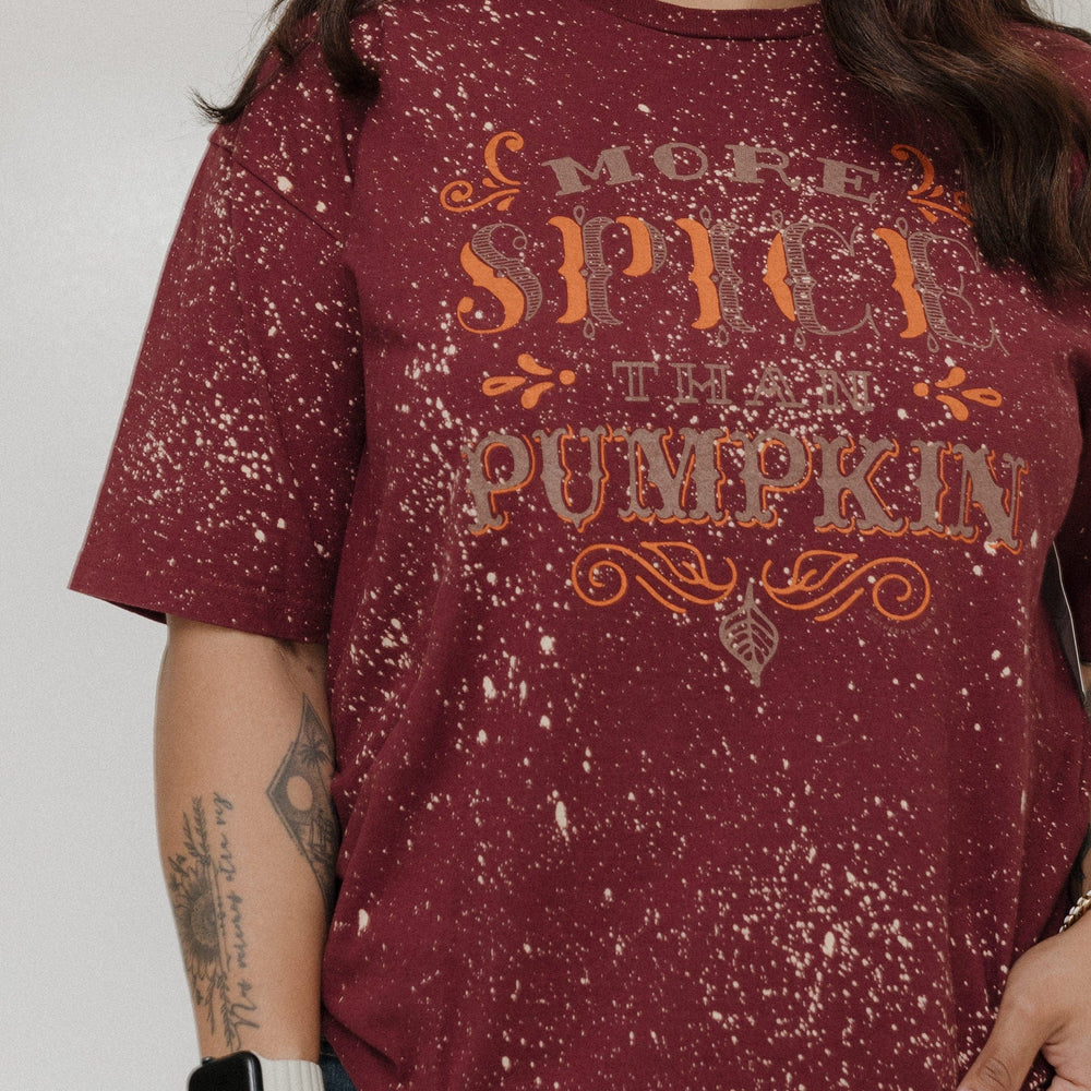 "MORE SPICE THAN PUMPKIN" GRAPHIC TEE Woman wearing a maroon shirt with 'More Spice Than Pumpkin' text on a plain background at Love Marlow