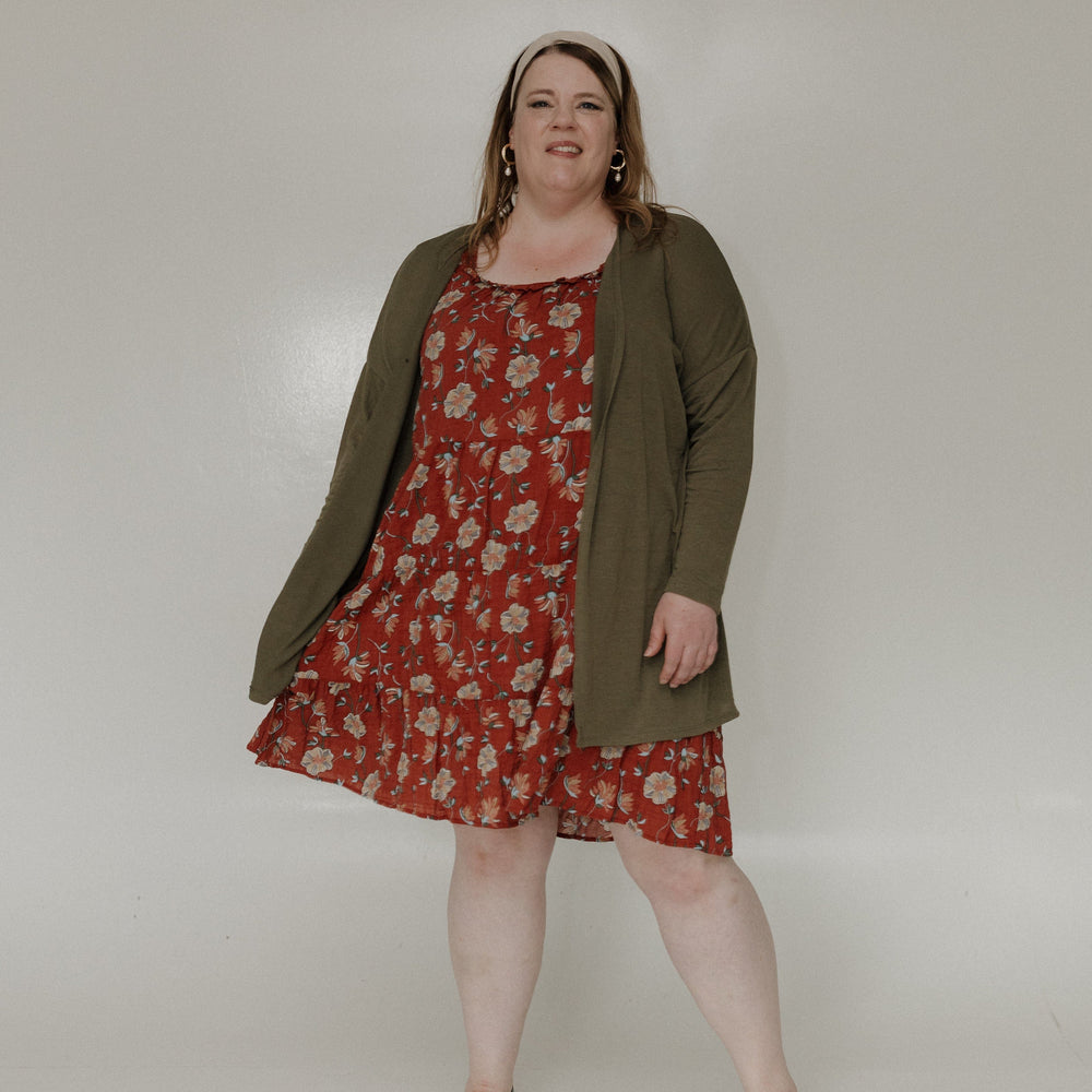 Woman wearing a red floral dress with an olive green cardigan against a white background