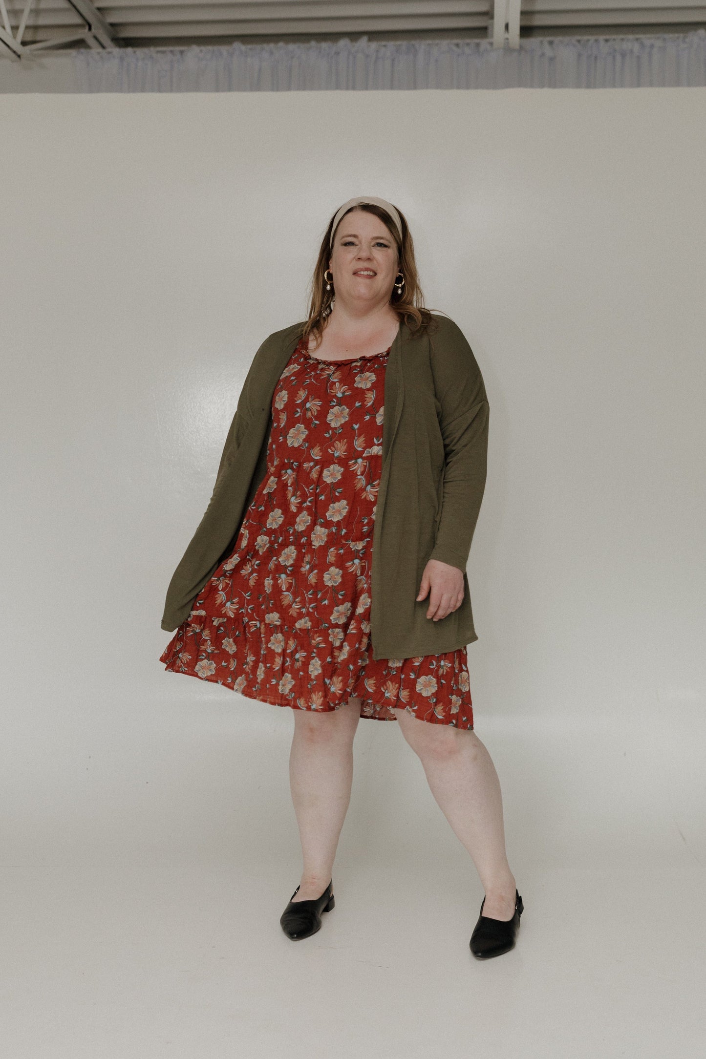 Woman wearing a red floral dress with an olive green cardigan against a white background