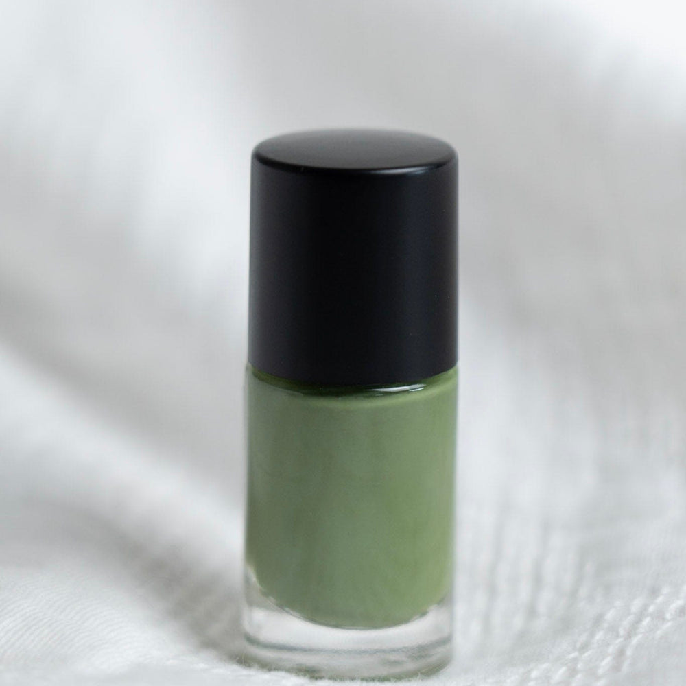 Green nail polish bottle with black cap on a white fabric background
