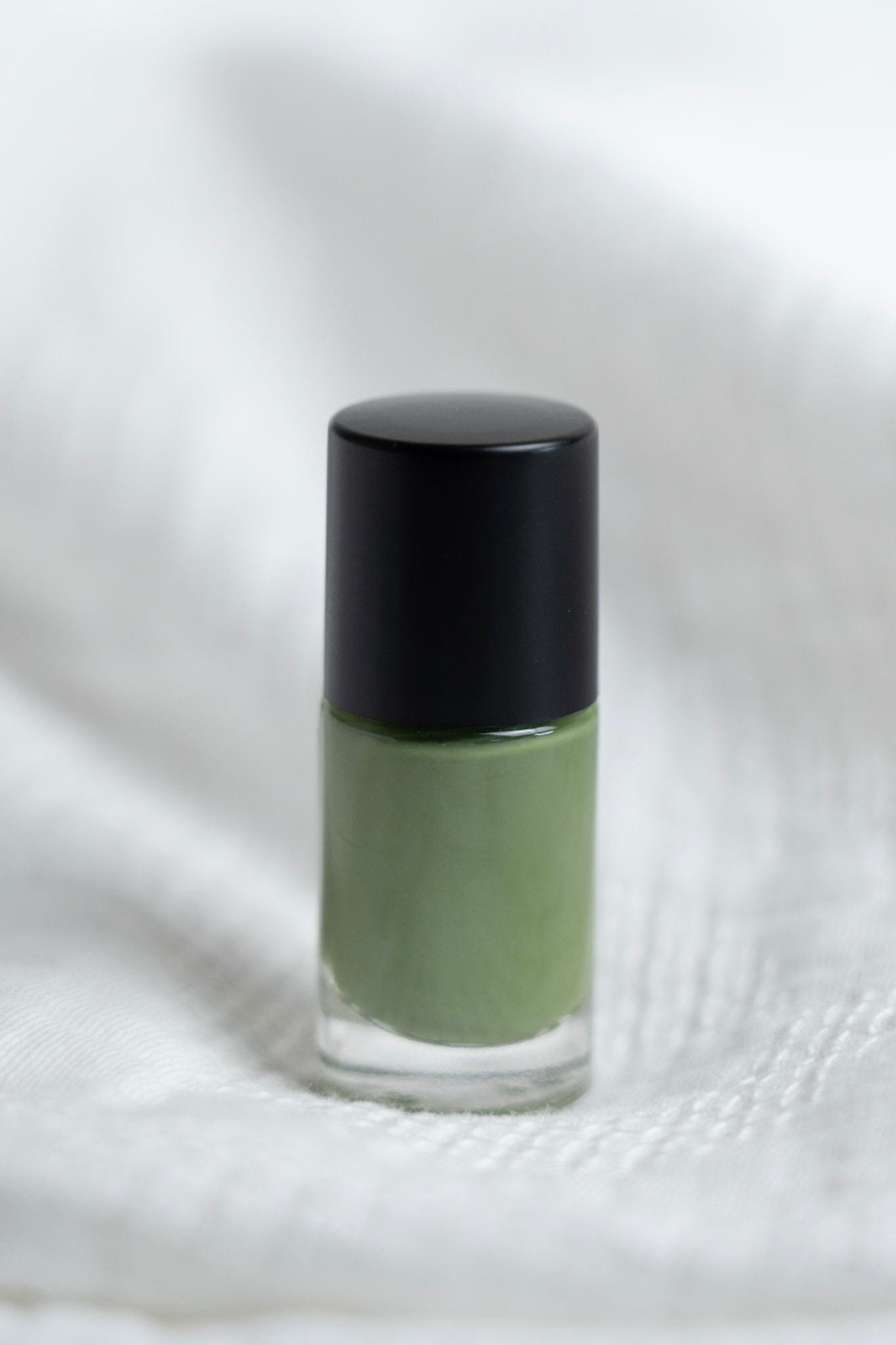 Green nail polish bottle with black cap on a white fabric background