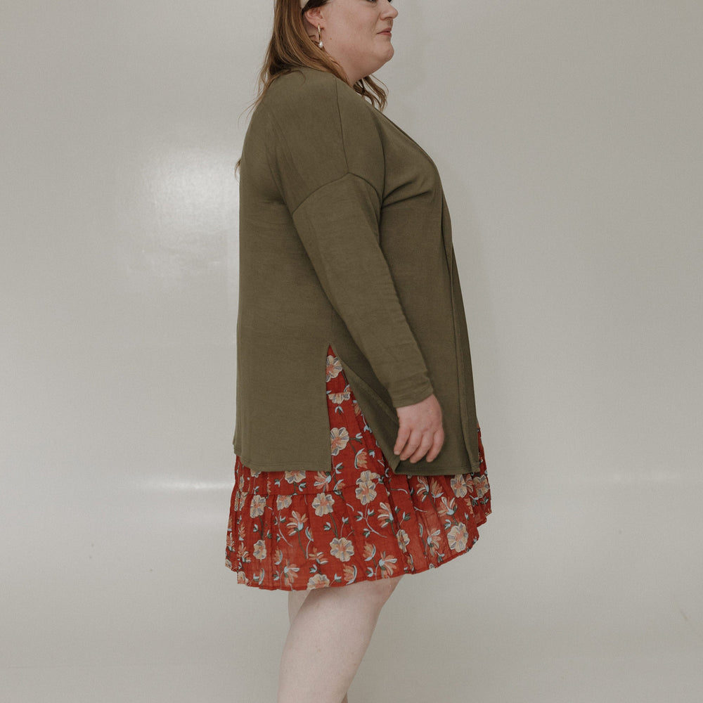 Woman wearing a green cardigan over a red floral dress on a white background