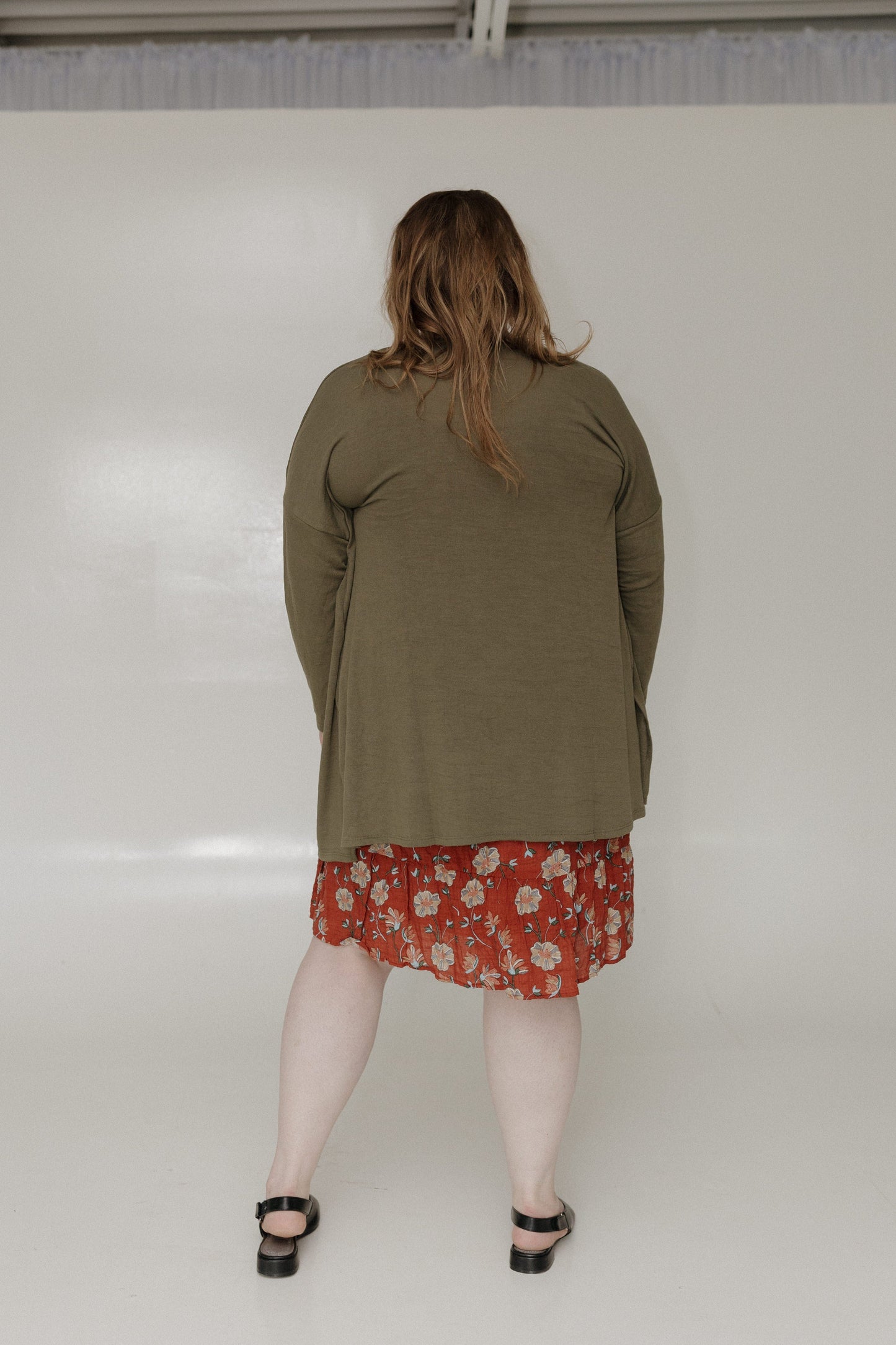 Person wearing a green jacket over a red floral skirt on a white background