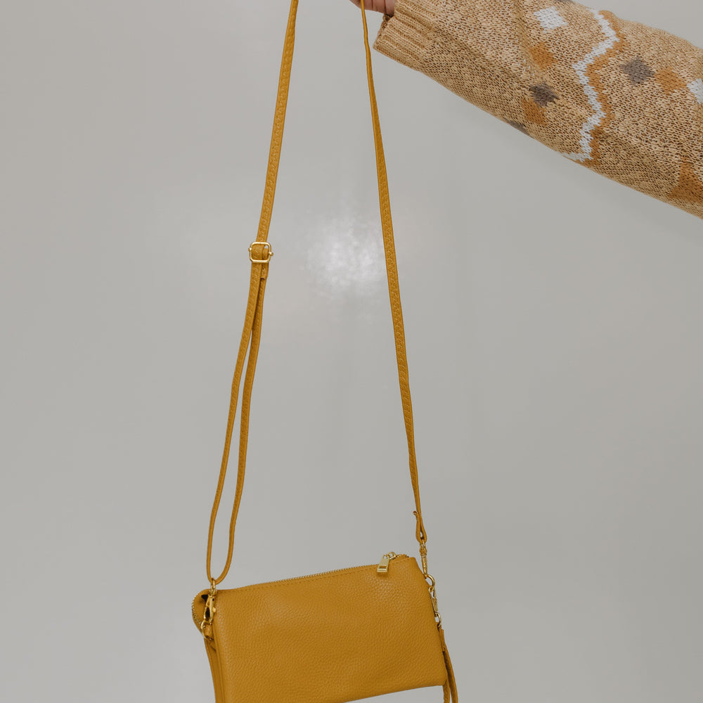 Mustard handbag held by a person against a plain background