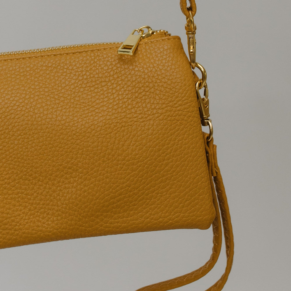 Mustard leather clutch bag with a strap on a gray background
