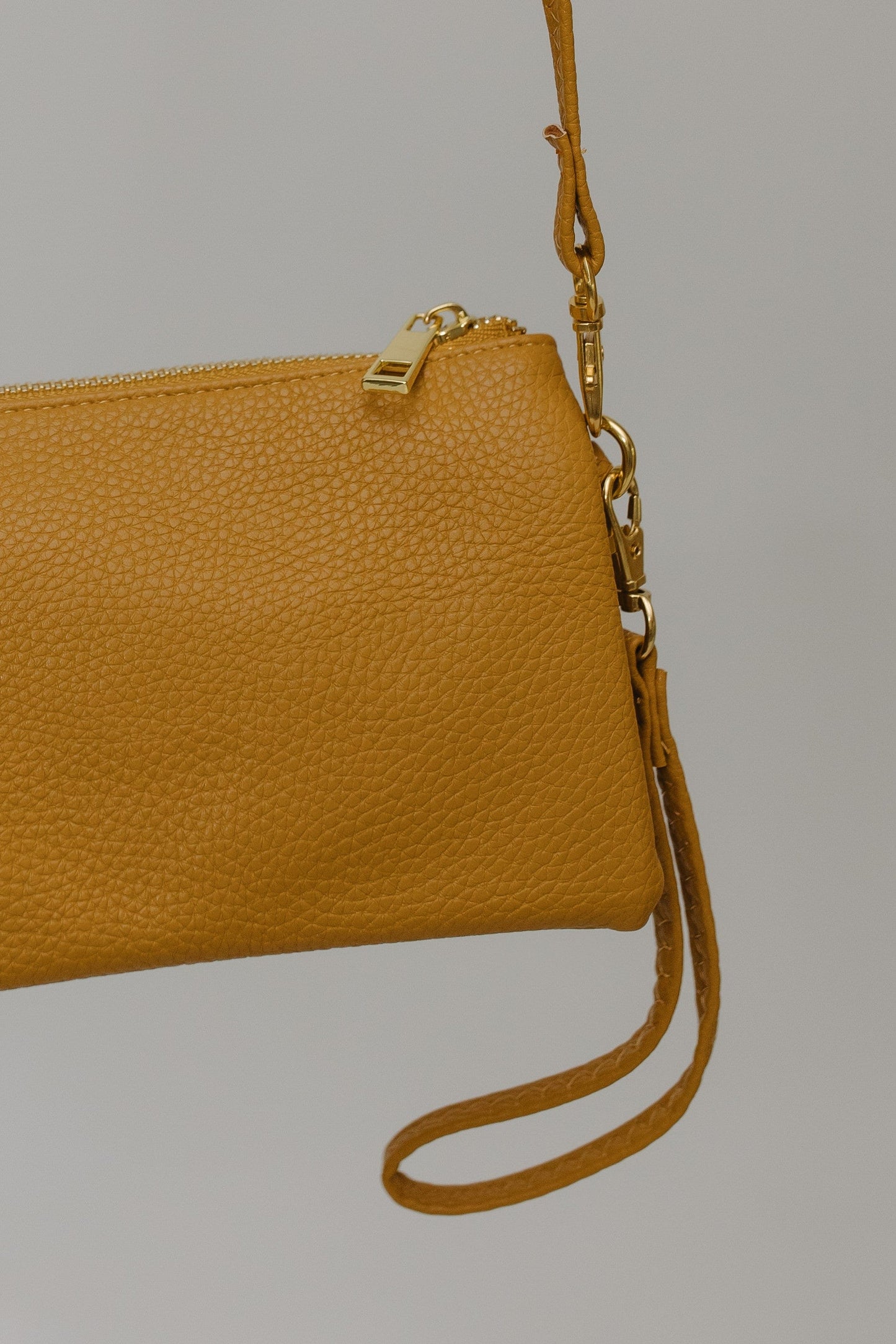 Mustard leather clutch bag with a strap on a gray background