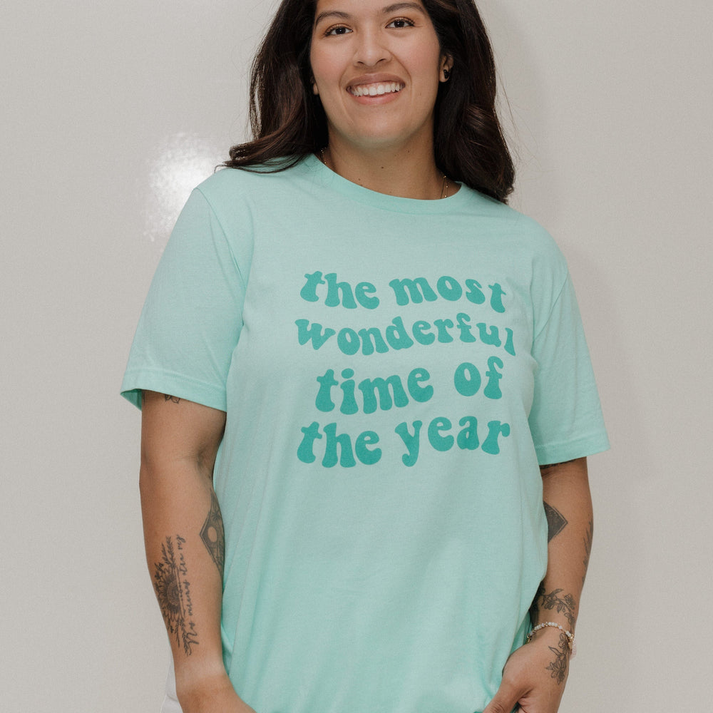 Person wearing a light blue t-shirt with text, standing against a plain background
