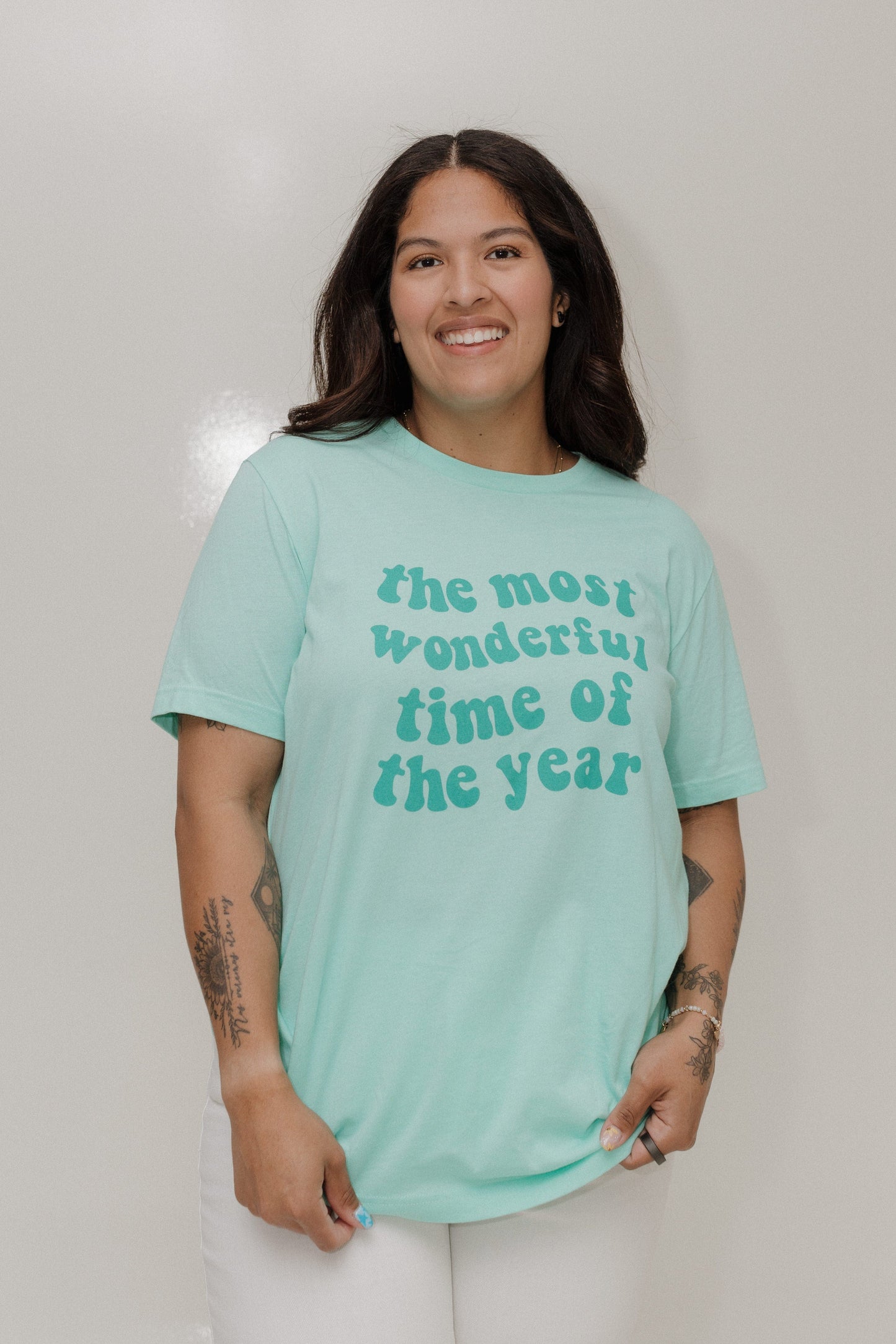 Person wearing a light blue t-shirt with text, standing against a plain background
