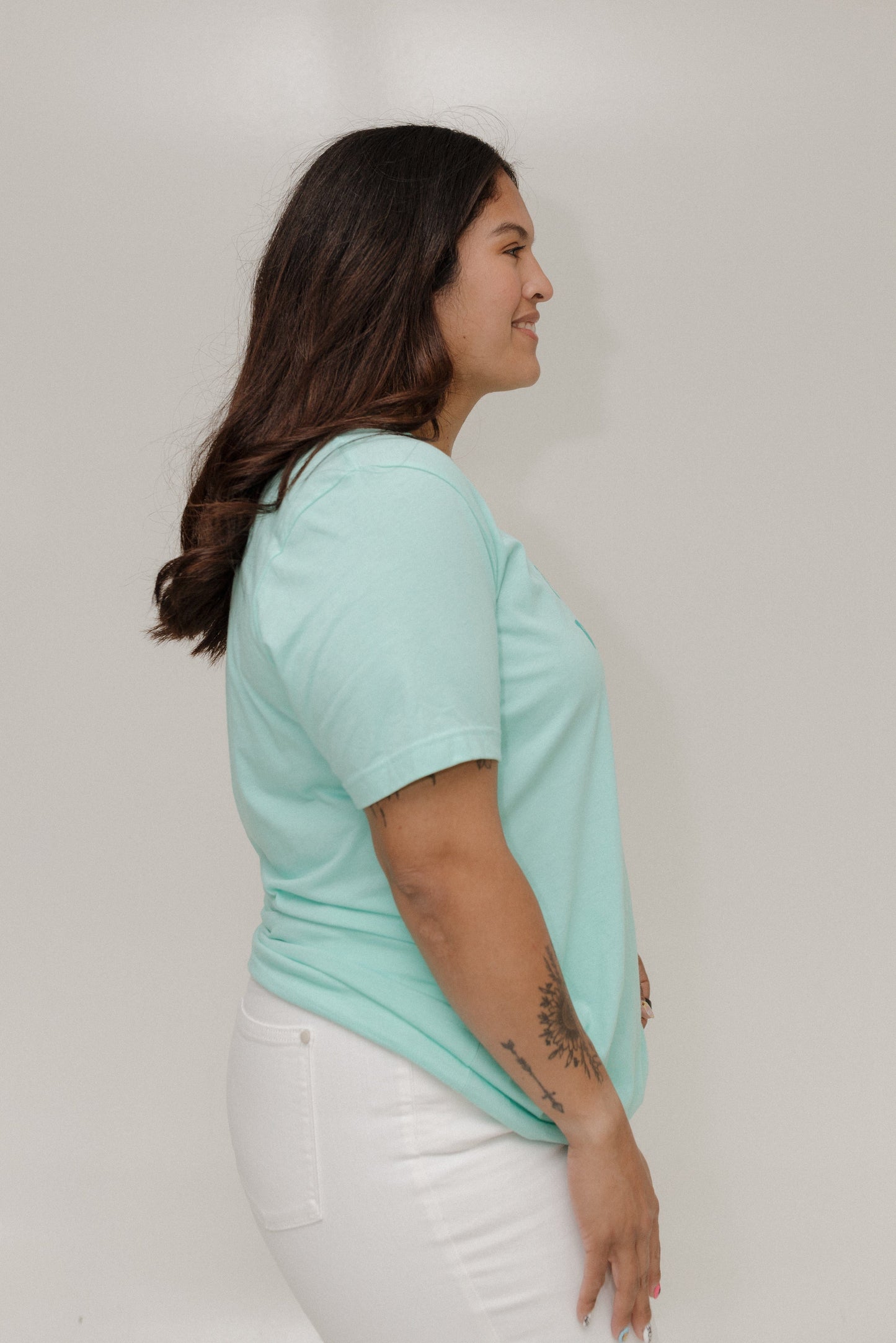 Woman wearing a light blue t-shirt and white pants against a plain background