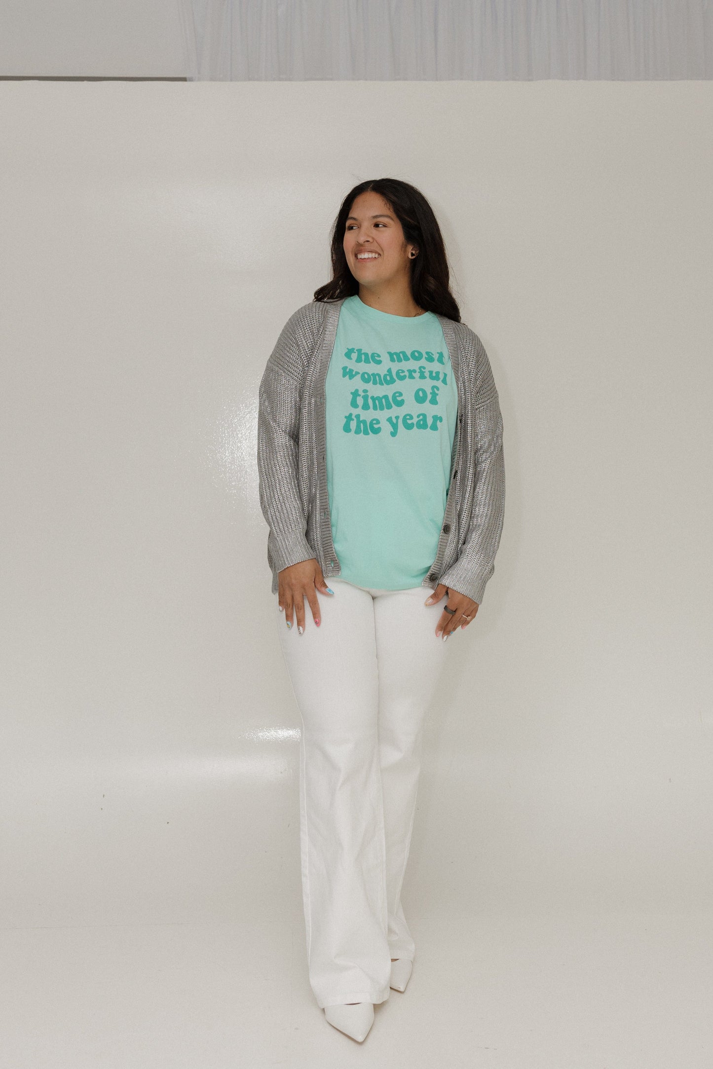 Woman wearing a light blue t-shirt with text and gray cardigan, standing against a white background