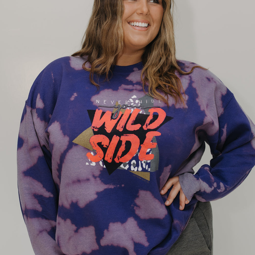 Person wearing a tie-dye sweatshirt with 'Wild Side' text against a plain background