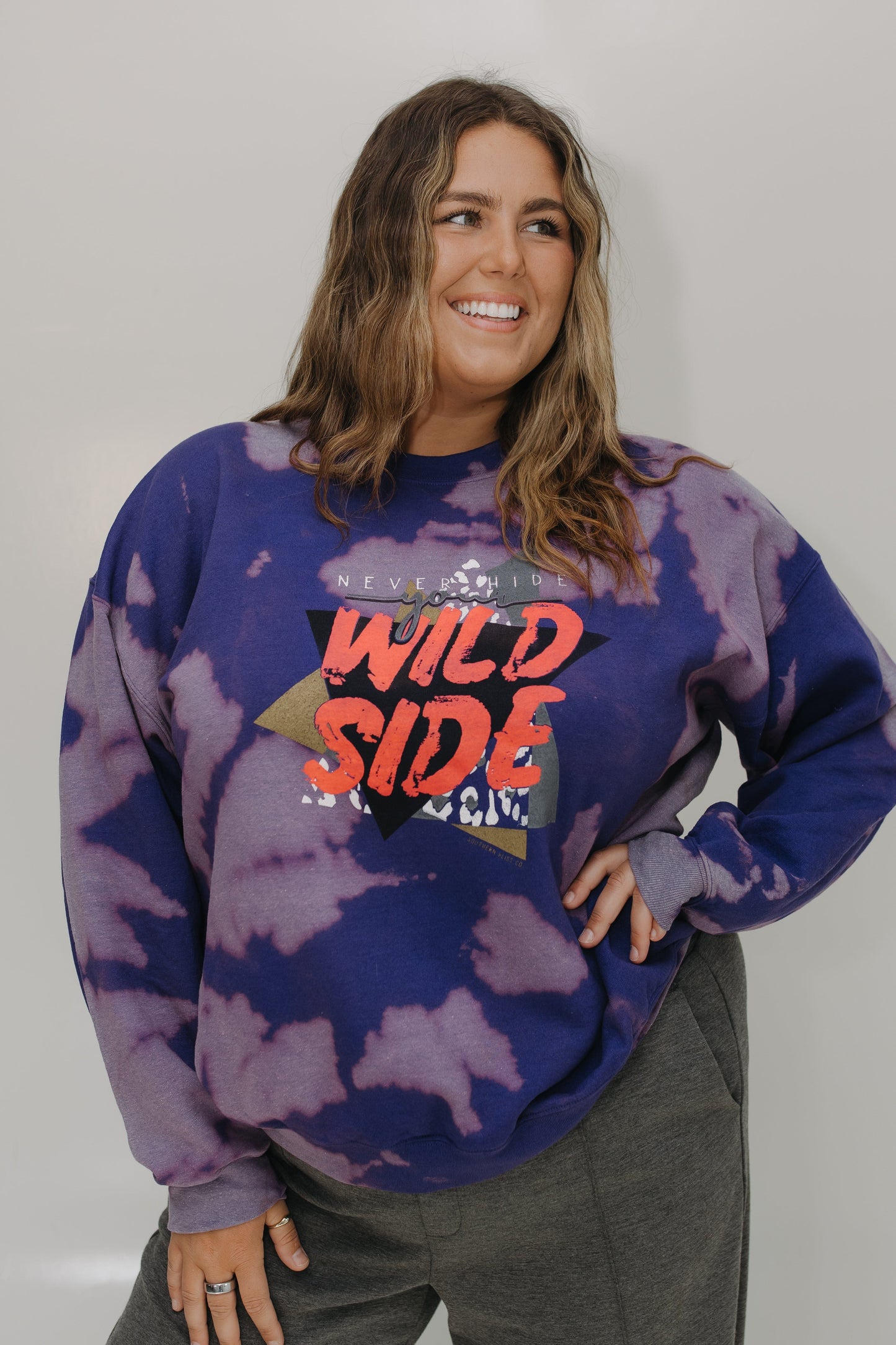 Person wearing a tie-dye sweatshirt with 'Wild Side' text against a plain background