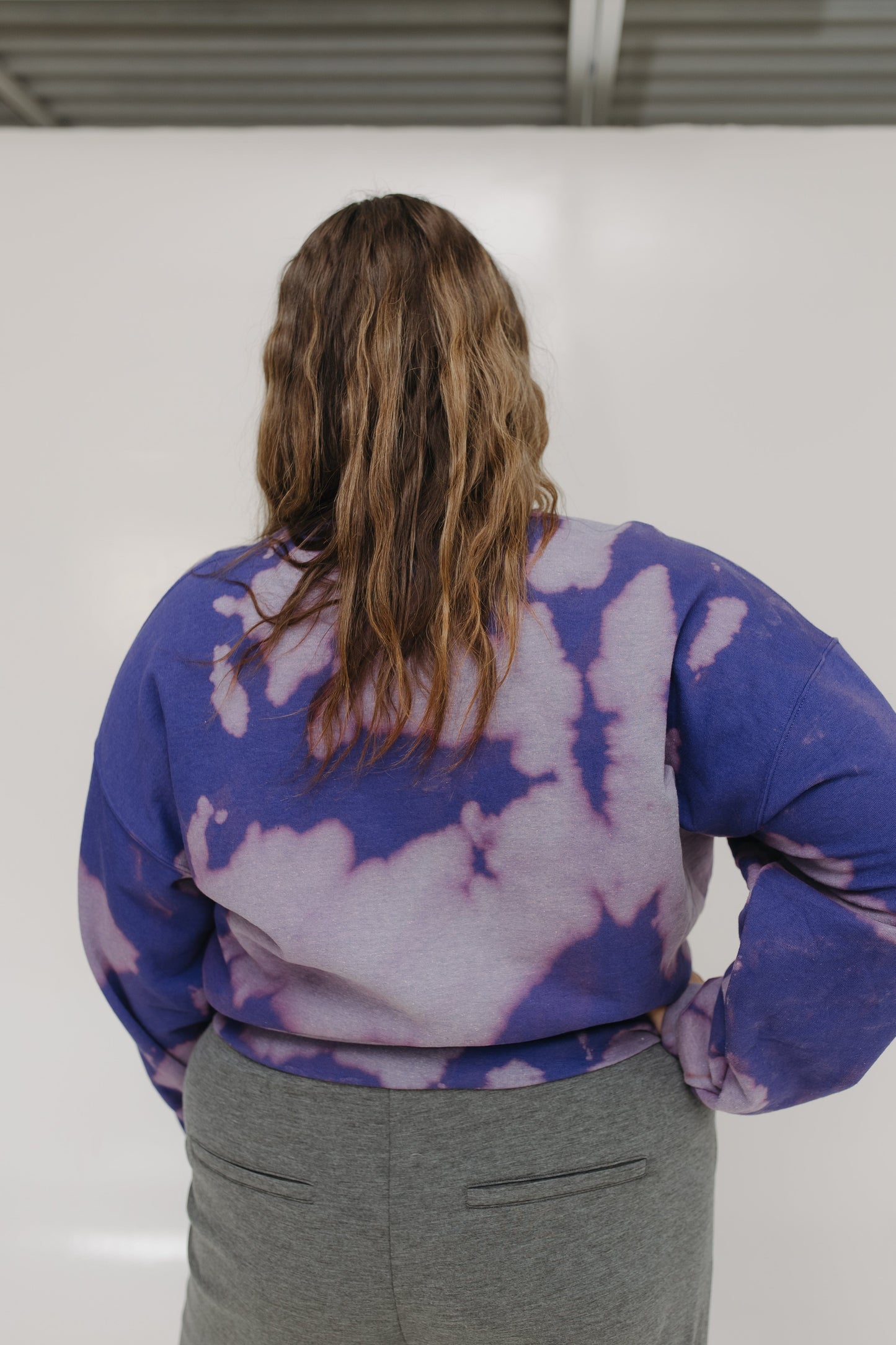 Person wearing a tie-dye shirt with purple and white patterns on a plain background