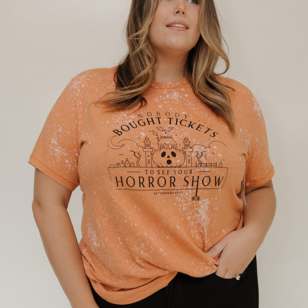 "NOBODY BOUGHT TICKETS TO SEE YOUR HORROR SHOW" GRAPHIC TEE Woman wearing an orange t-shirt with a graphic design at Love Marlow