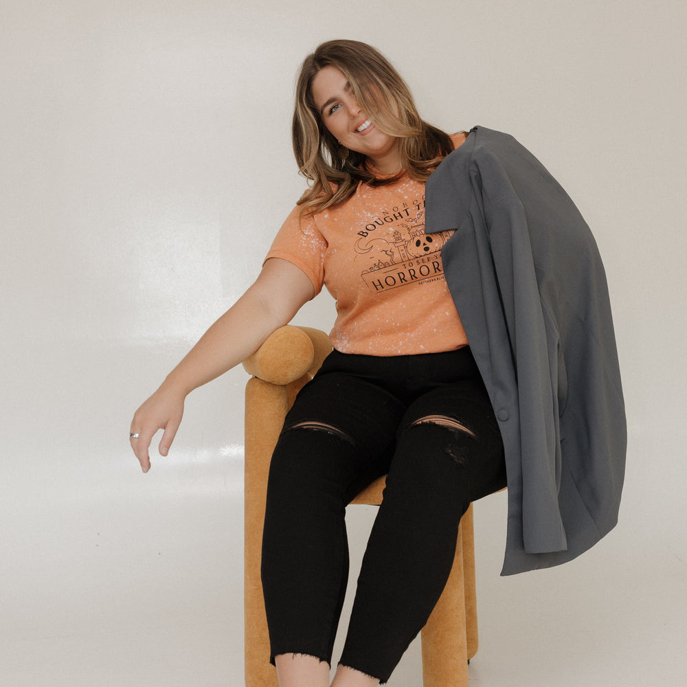 "NOBODY BOUGHT TICKETS TO SEE YOUR HORROR SHOW" GRAPHIC TEE Woman wearing an orange t-shirt with a graphic design at Love Marlow