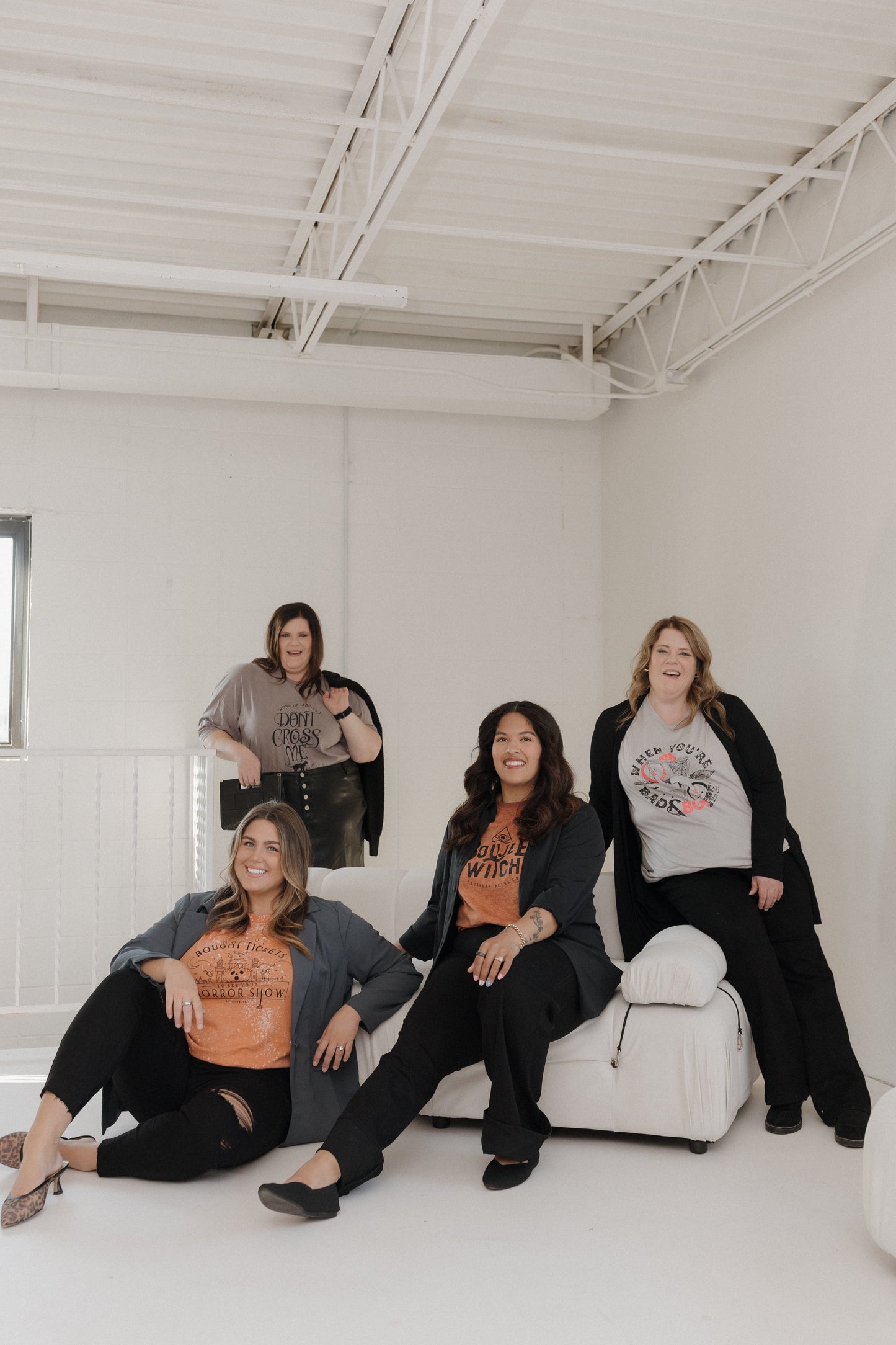 Four women posing together in a white room wearing graphic Halloween and fall t-shirts at Love Marlow