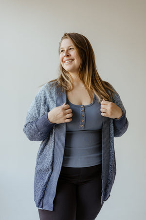 A woman smiling and holding her Ombre Textured Cardigan with Striped Collar Detail by Yesta, perfect for any work wardrobe.