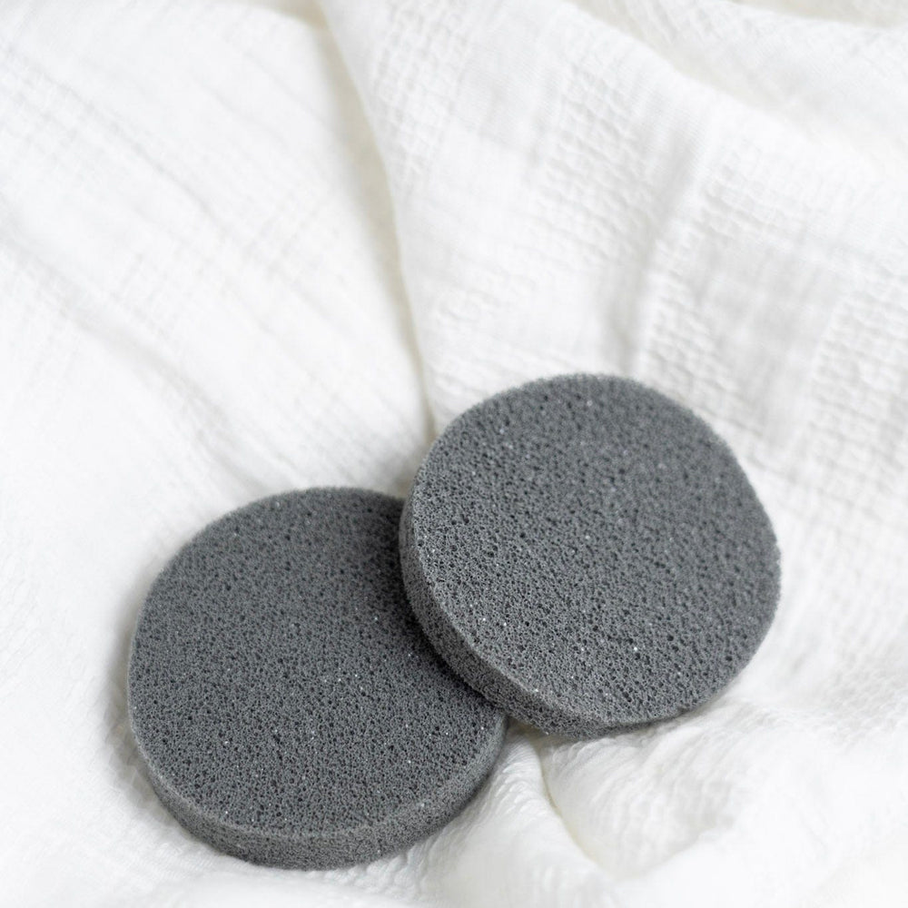 Two gray deodorant removers on a white textured fabric background