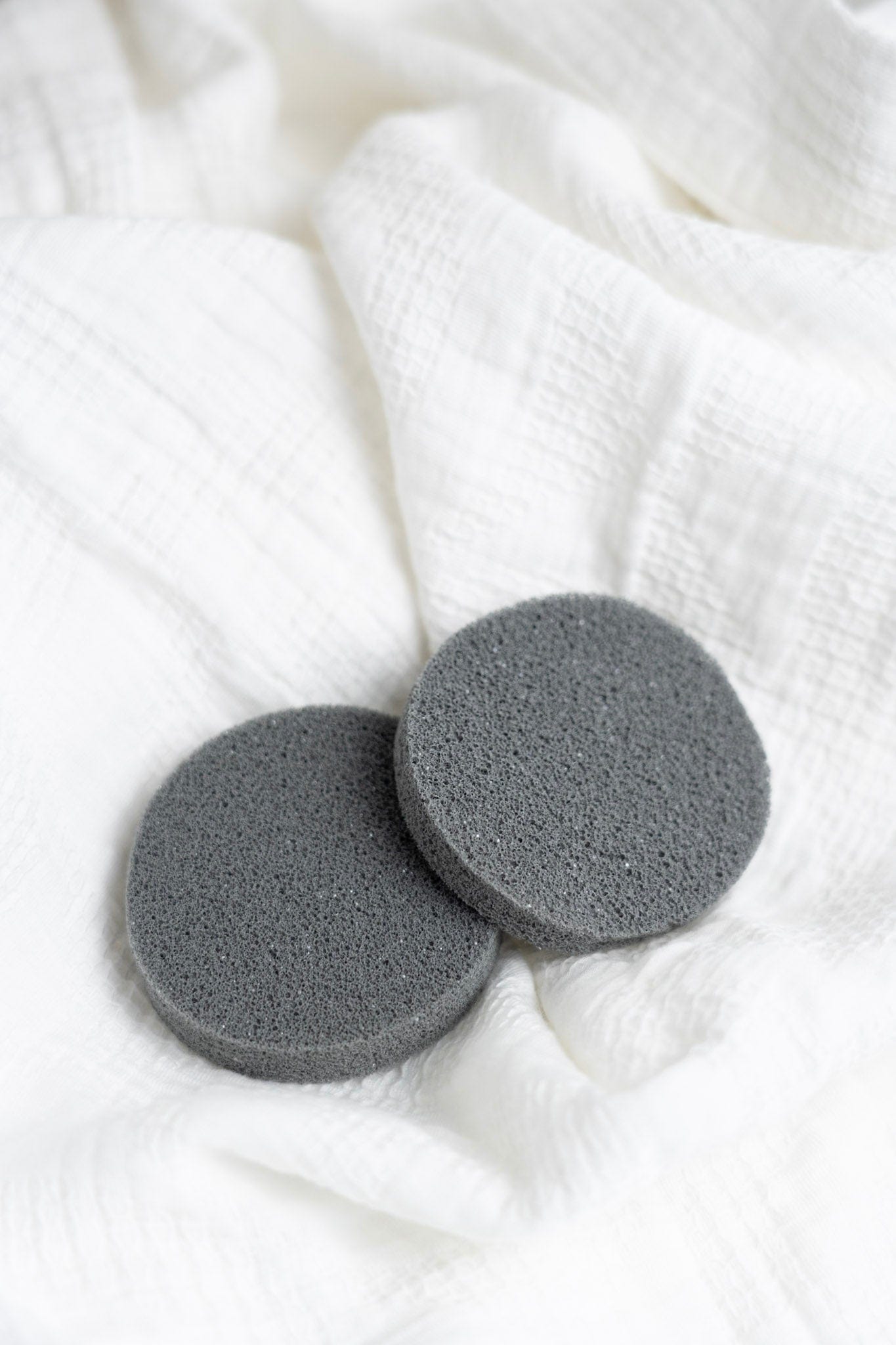 Two gray deodorant removers on a white textured fabric background