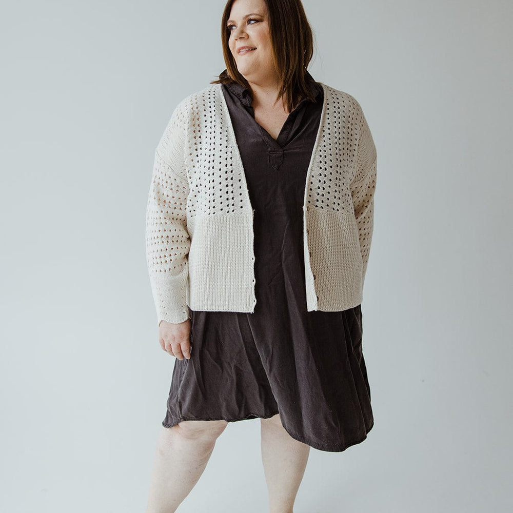 A person stands against a plain background, wearing a dark dress, black shoes, and an **Open Weave Knit Cardigan** by **Love Marlow**, featuring wooden buttons.