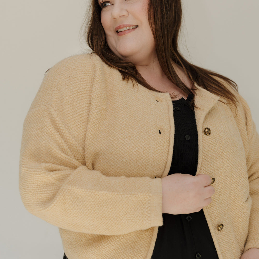 Woman wearing a beige cardigan over a black top against a plain background