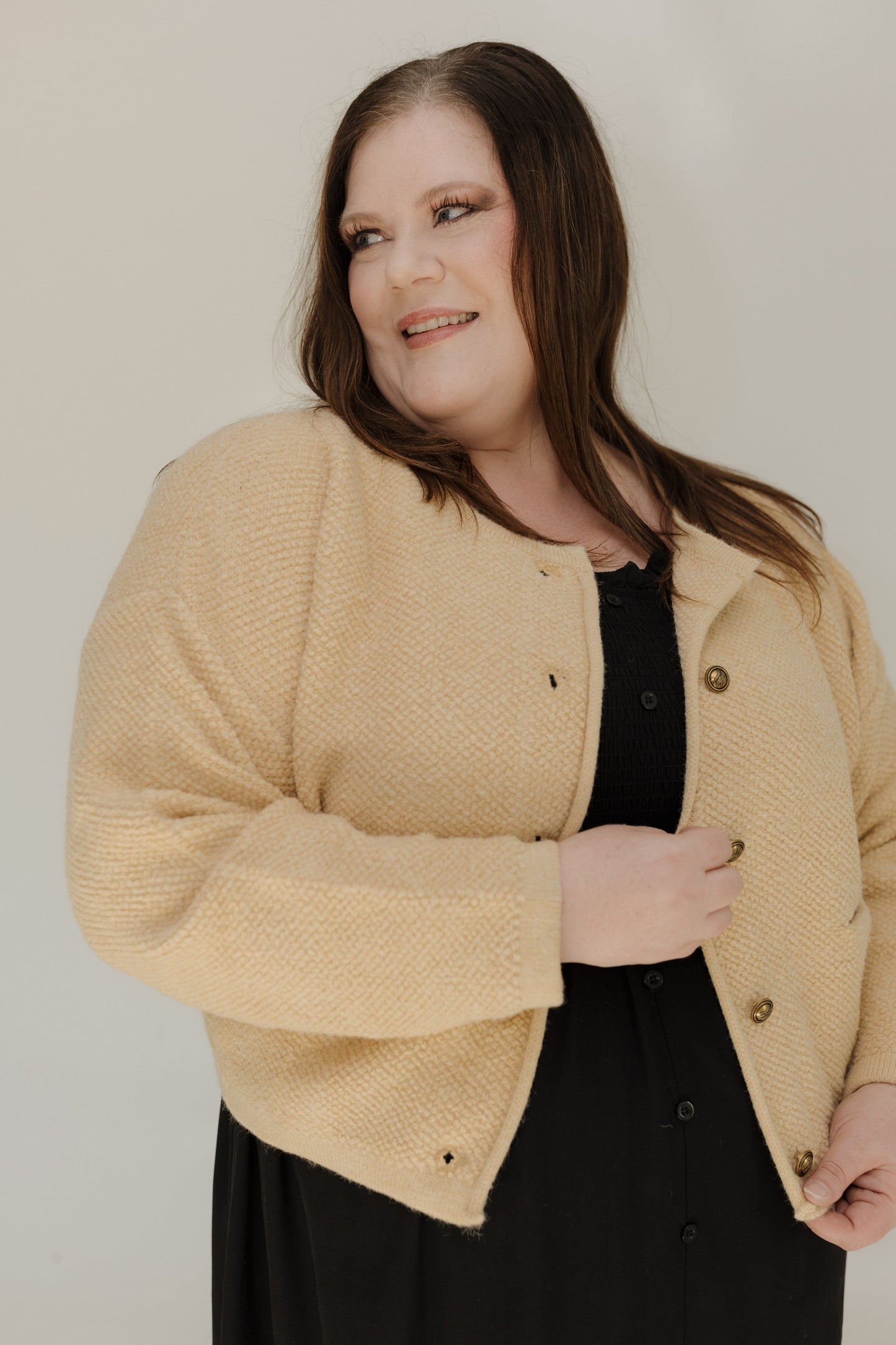 Woman wearing a beige cardigan over a black top against a plain background