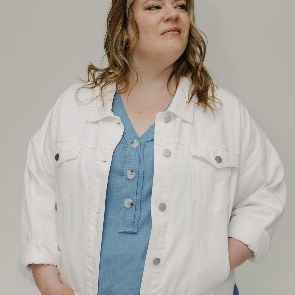 Woman wearing a white denim jacket over a blue shirt on a plain background